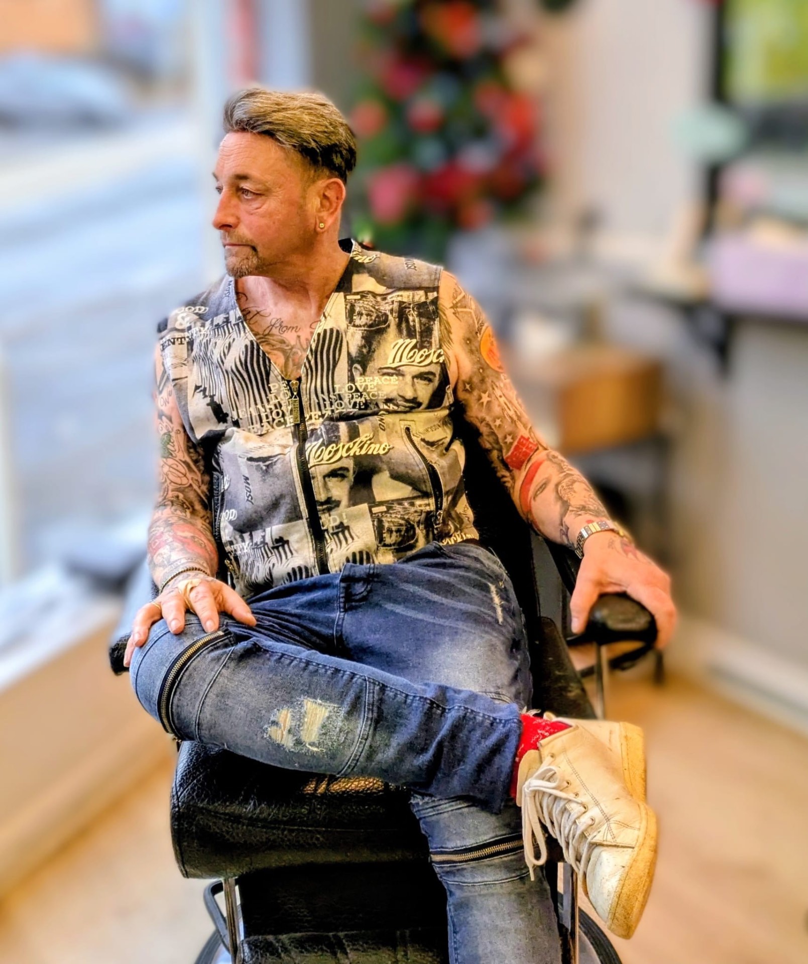 Sean seated in a barber's chair, sleeve tattoos on show